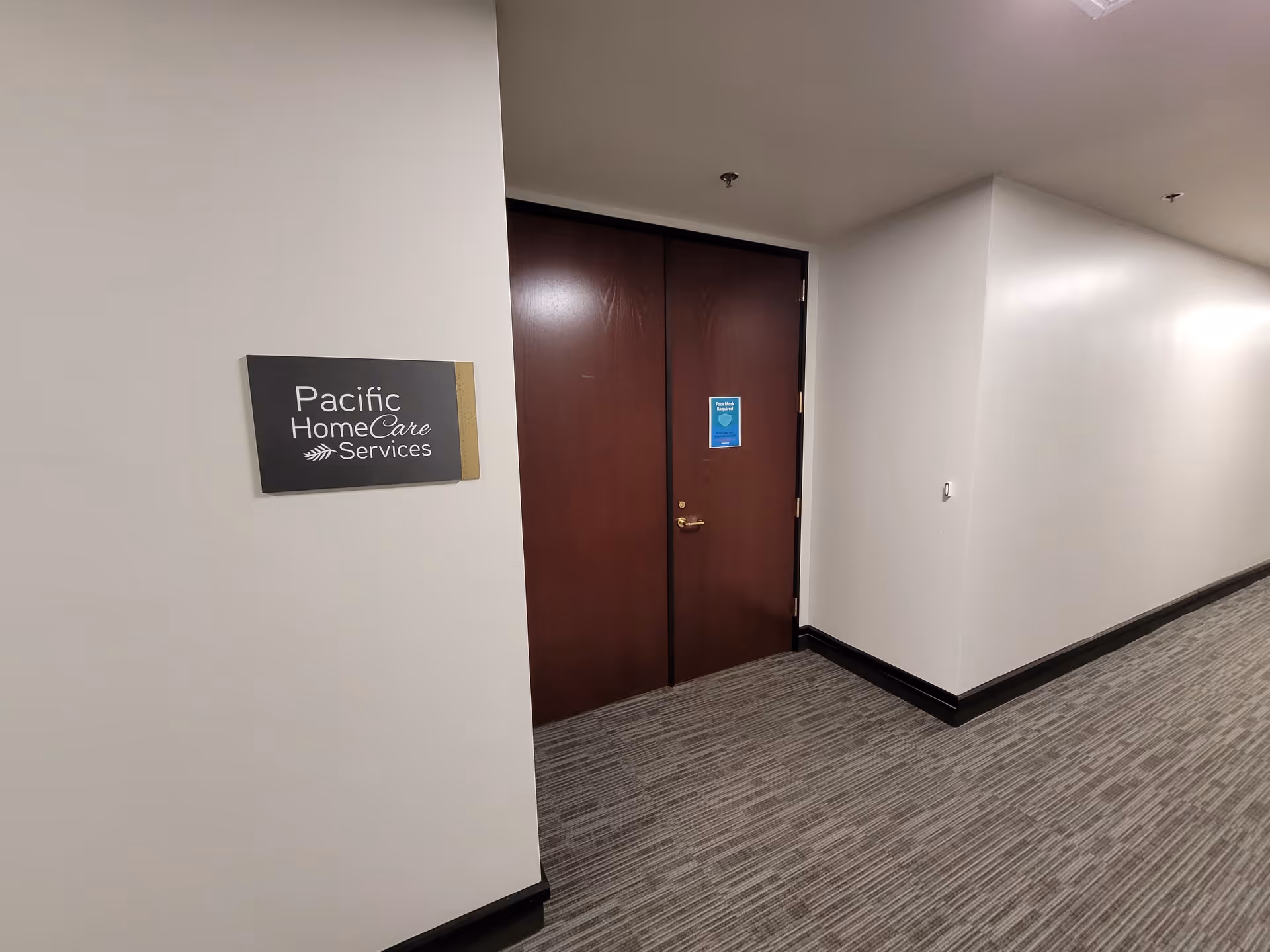 Hallway with dark double doors and a Pacific HomeCare Services sign on the wall.