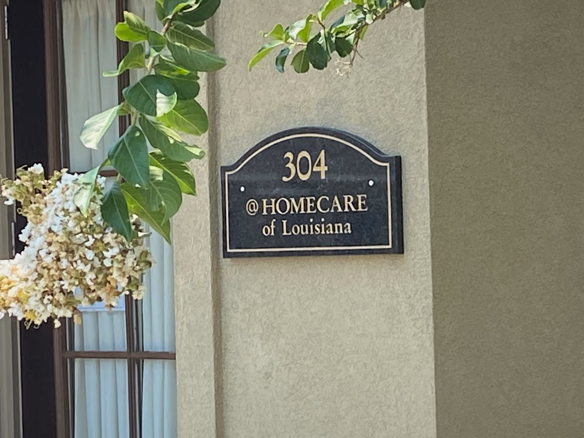 Exterior wall sign reading 304 @ Homecare of Louisiana with greenery nearby.