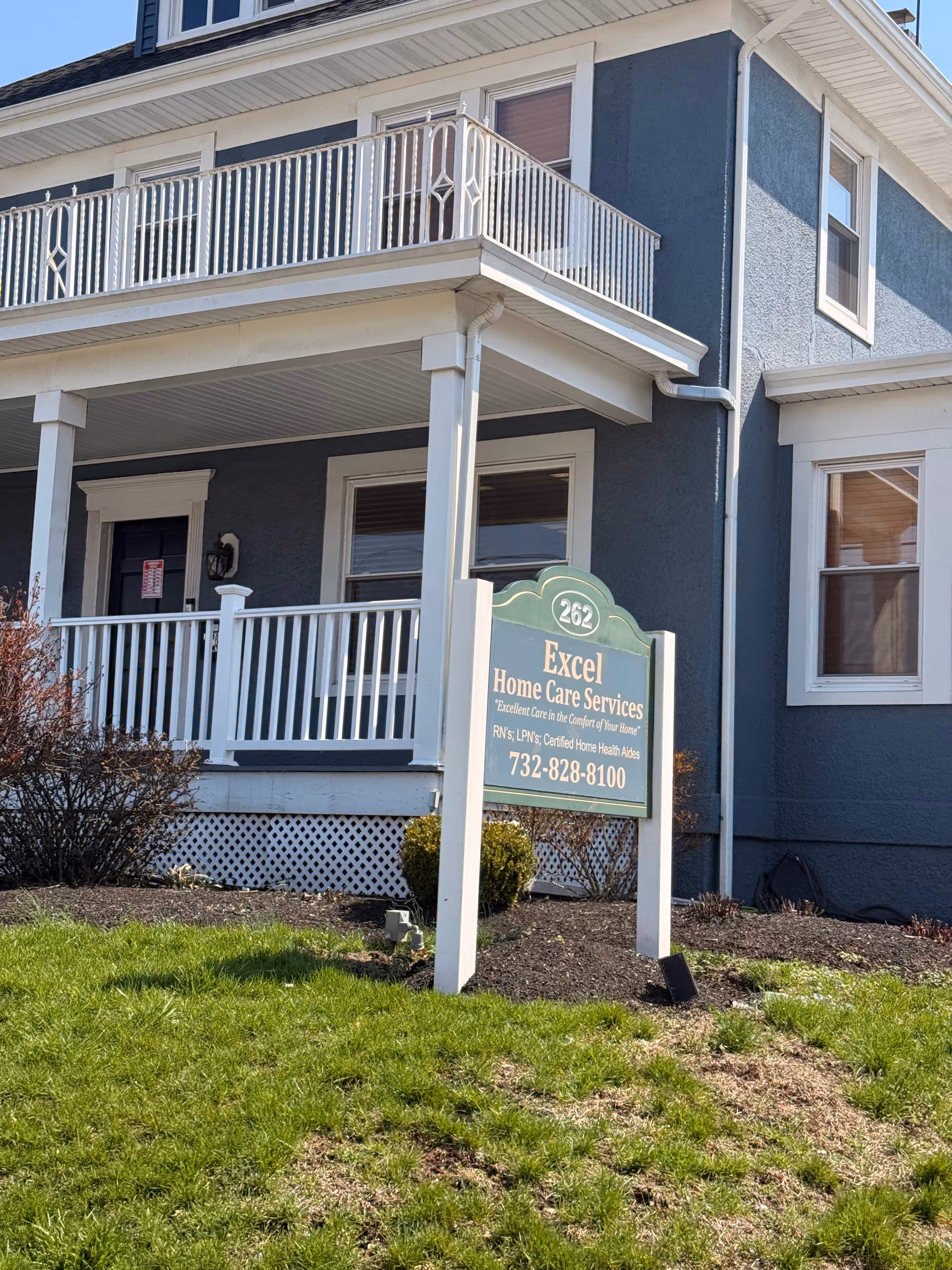 Two-story blue building with a white balcony and a sign for Excel Home Care Services