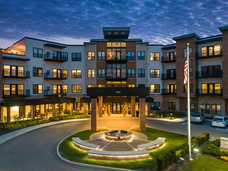 Exterior view of Rose Senior Living Carmel building entrance with circular fountain and flag