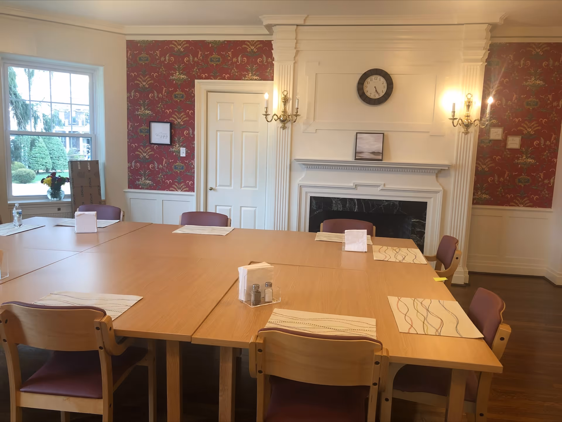 Large wooden dining table with placemats in a formal, wallpapered dining room.