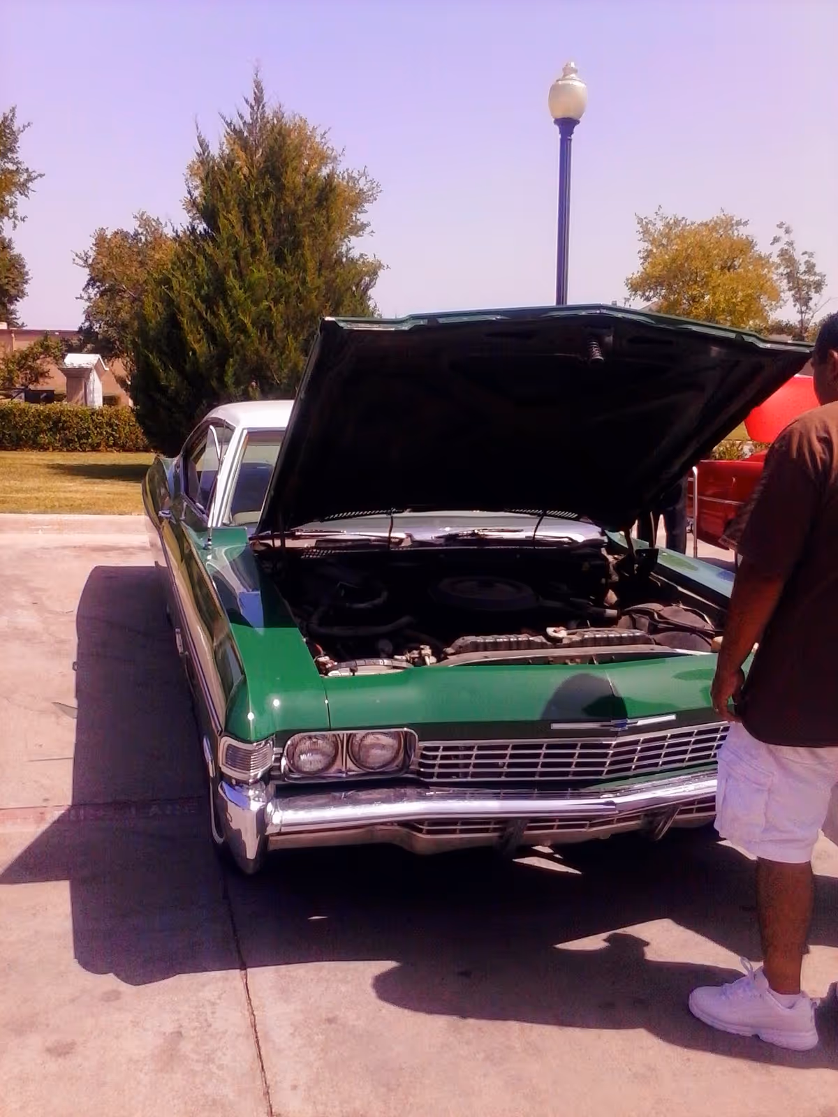 Green vintage car with hood open parked in a lot, nearby man.