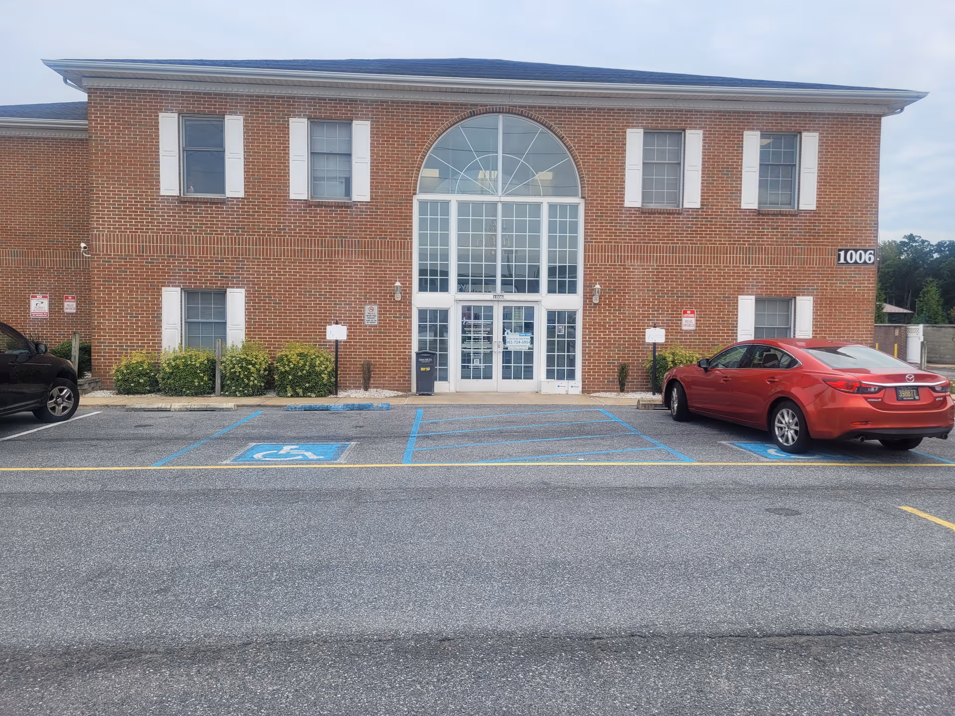 Brick senior living facility with a large arched glass entrance and handicap parking.