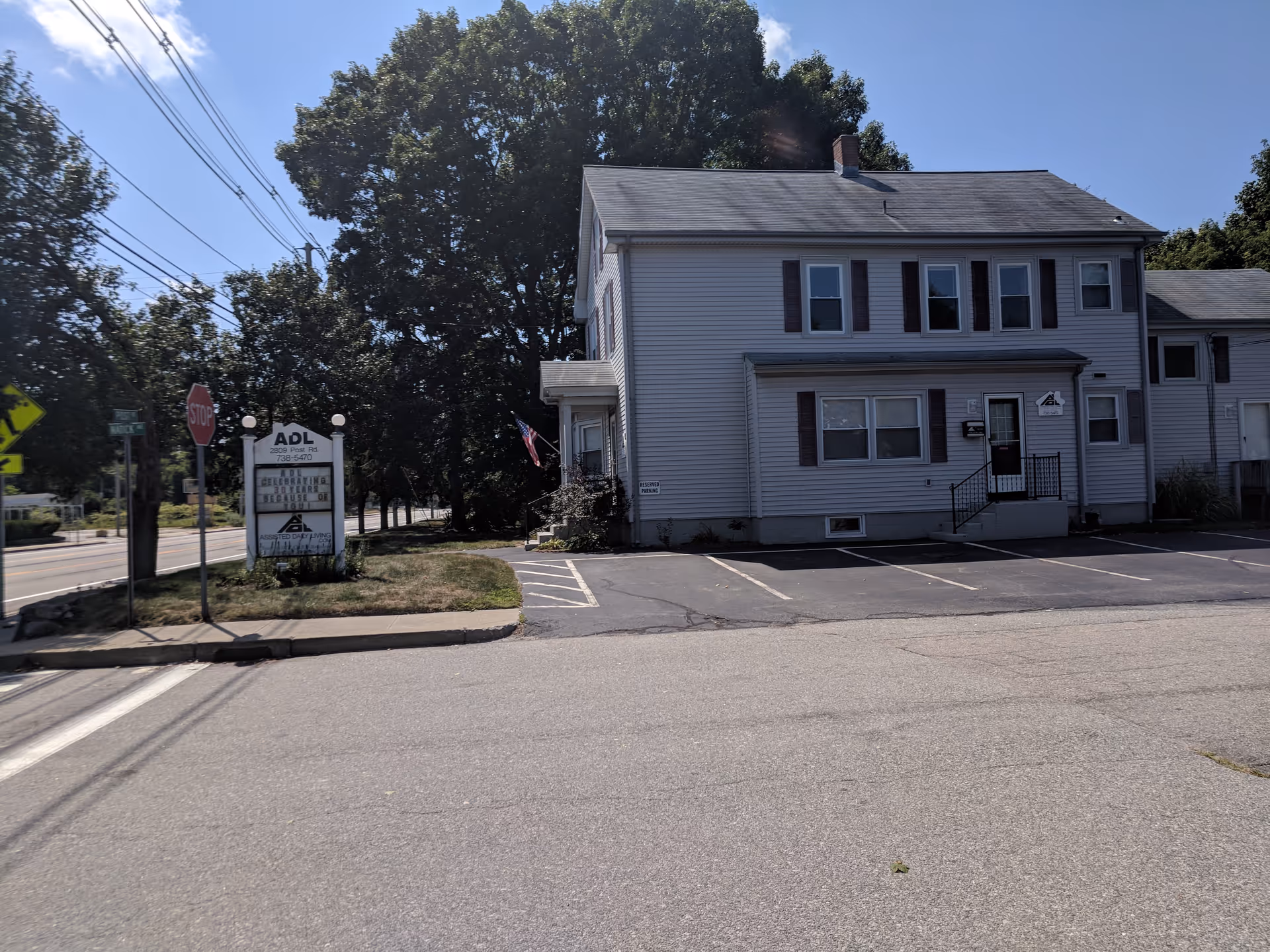 A two-story gray Assisted Daily Living building with a parking lot along a street.