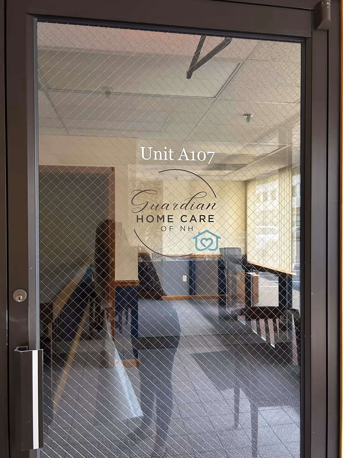 Glass door displays Unit A107 and Guardian Home Care of NH logo inside a hallway