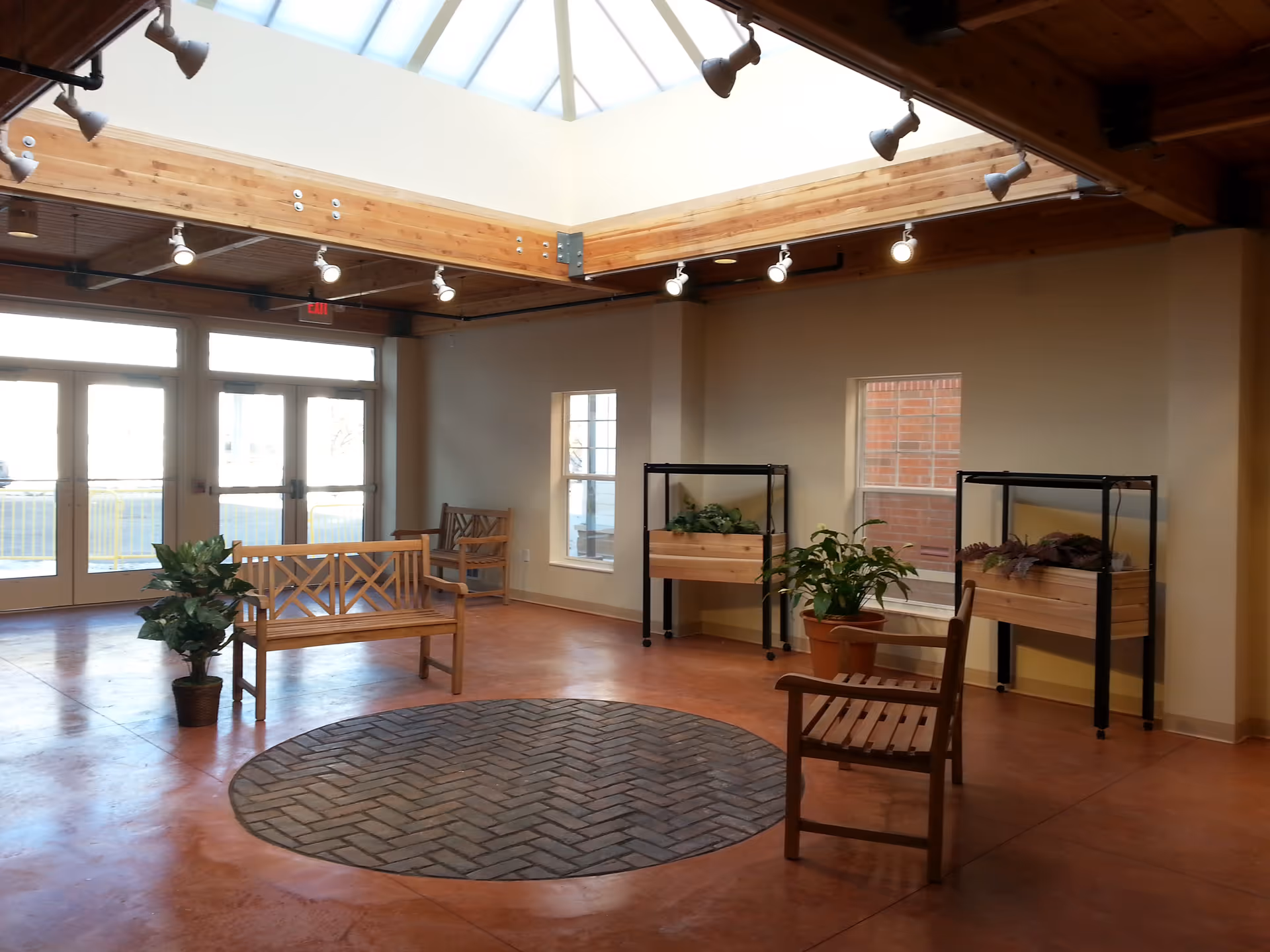 Spacious indoor lounge with wooden benches, planters, skylight, and brick exterior visible through windows.