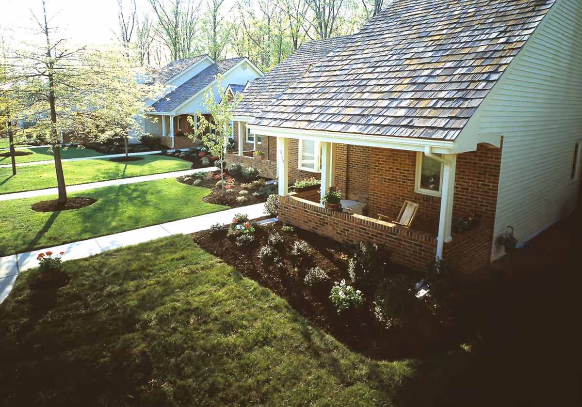Exterior view of brick cottages with porches, green lawn, and winding sidewalks in a landscaped campus.