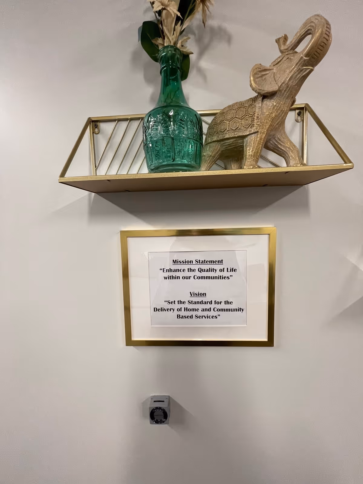 Decorative wall shelf with a green bottle, elephant sculpture, and framed mission statement.