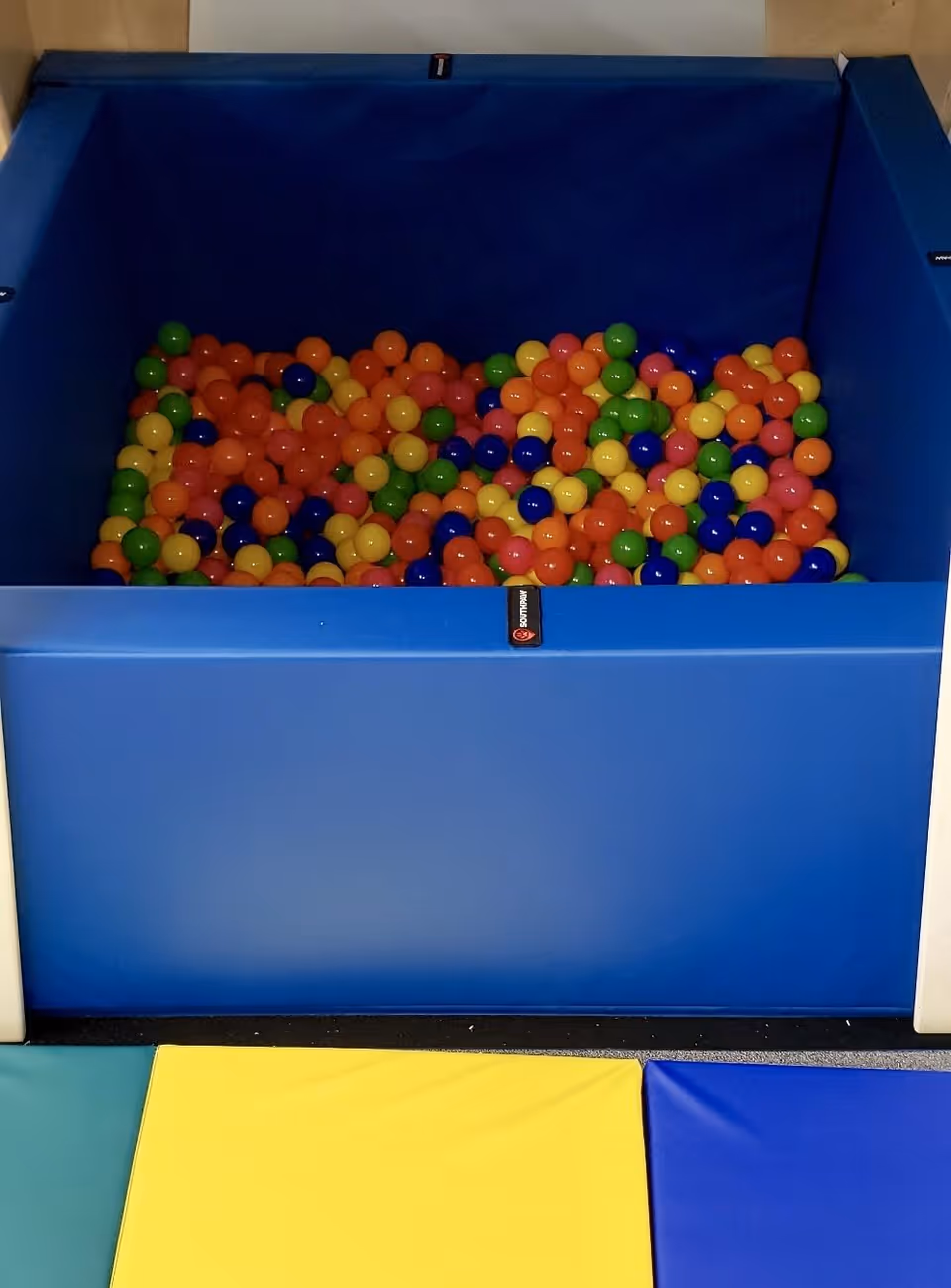 Blue ball pit filled with colorful plastic balls inside a padded play area.
