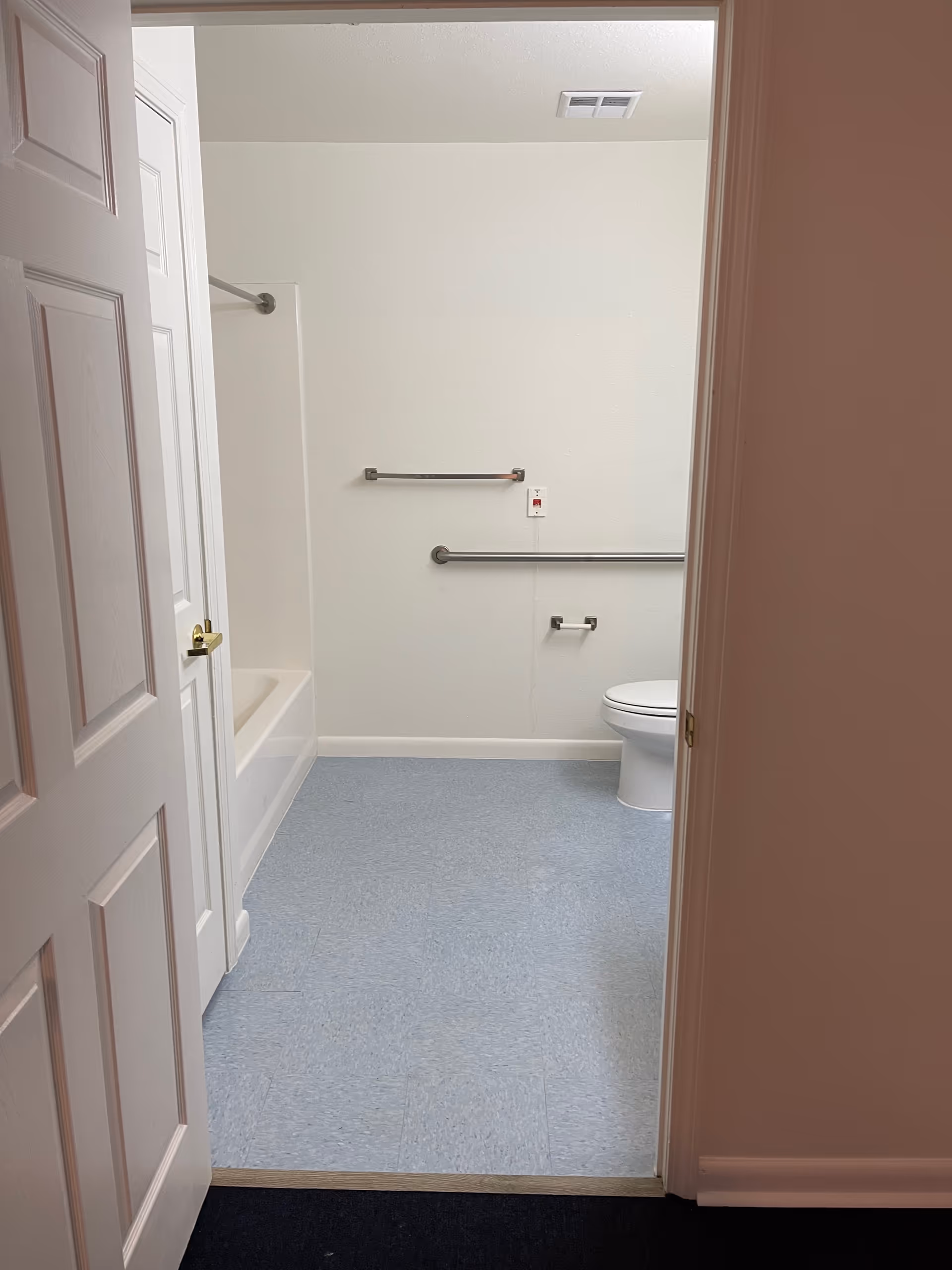 View of a clean bathroom with a bathtub, toilet, and accessibility rails.