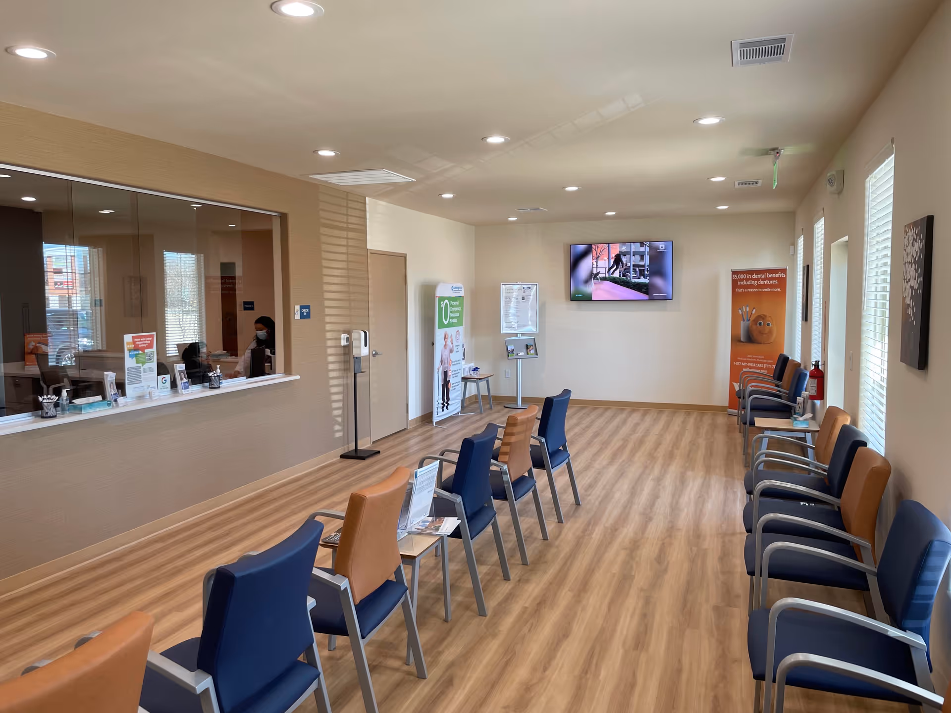 Spacious waiting area with blue and tan chairs, a reception desk, and a wall-mounted TV.