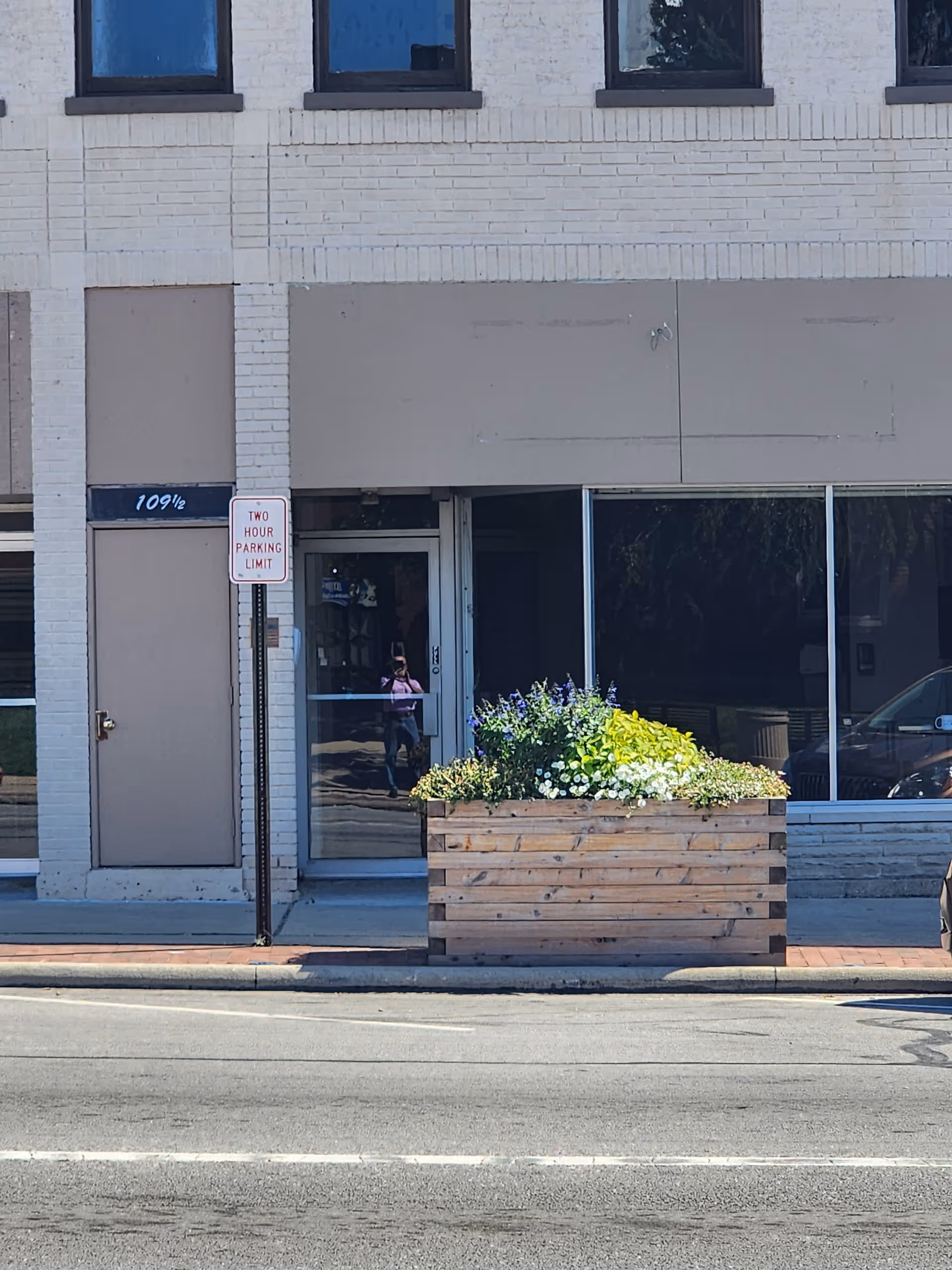 Storefront with glass doors, planter box, and two-hour parking sign on sidewalk.