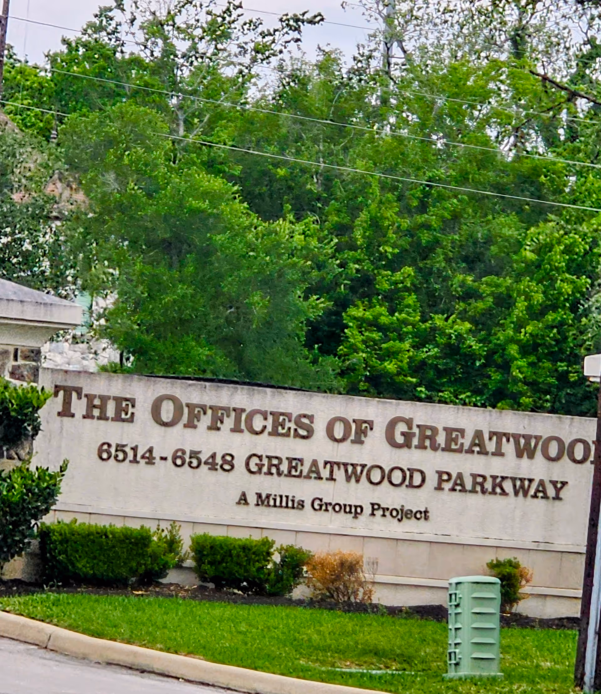 Exterior view of a stone sign reading 'The Offices of Greatwood Parkway' with greenery.