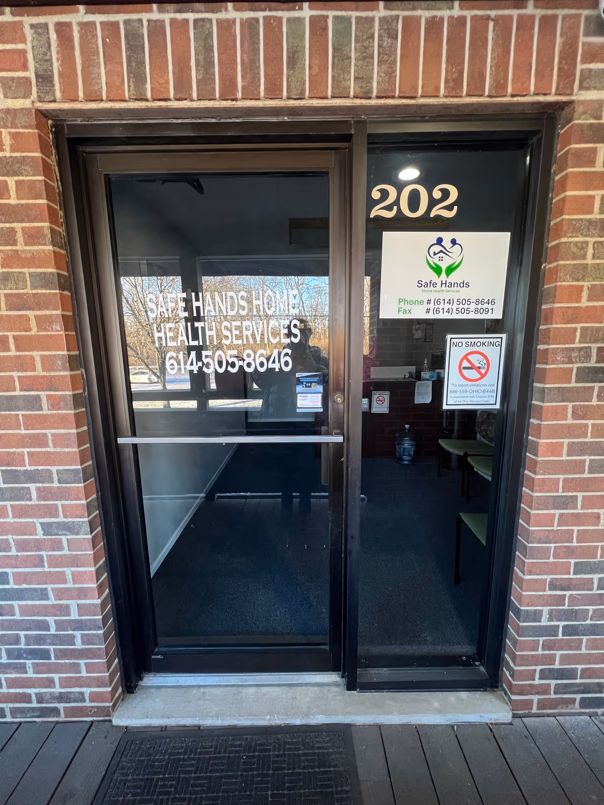 Glass entry door with brick exterior shows Safe Hands Home Health Services signage.