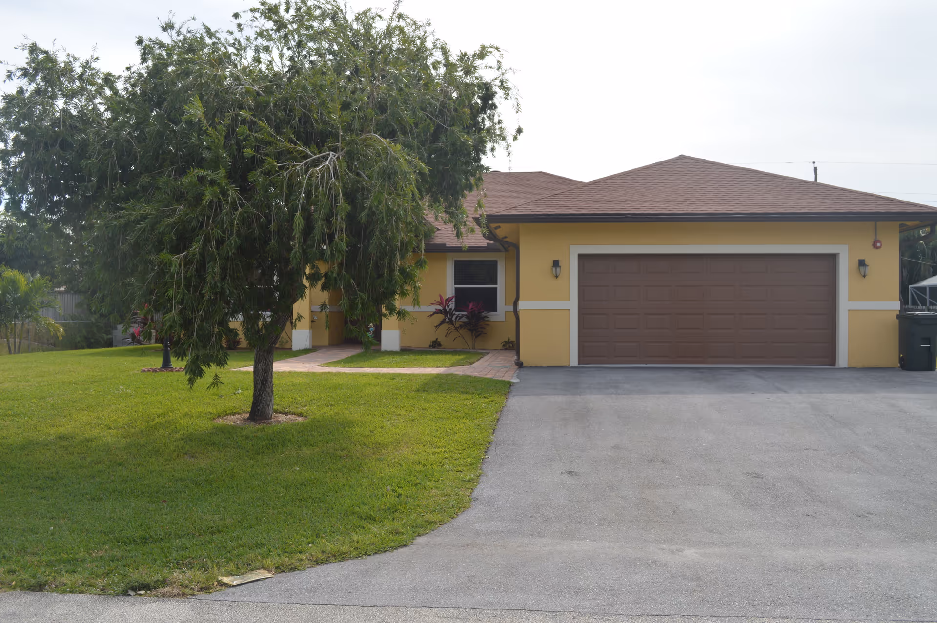 Yellow one-story house with a two-car garage, front lawn, and a tree.