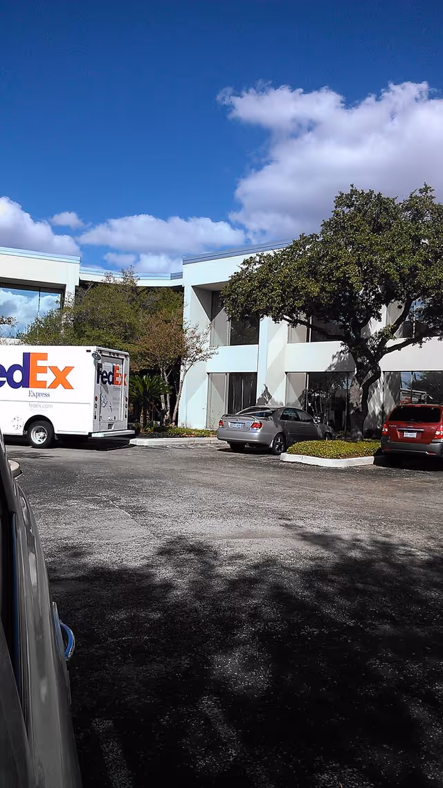 Exterior view of a facility with a FedEx truck and parked cars.