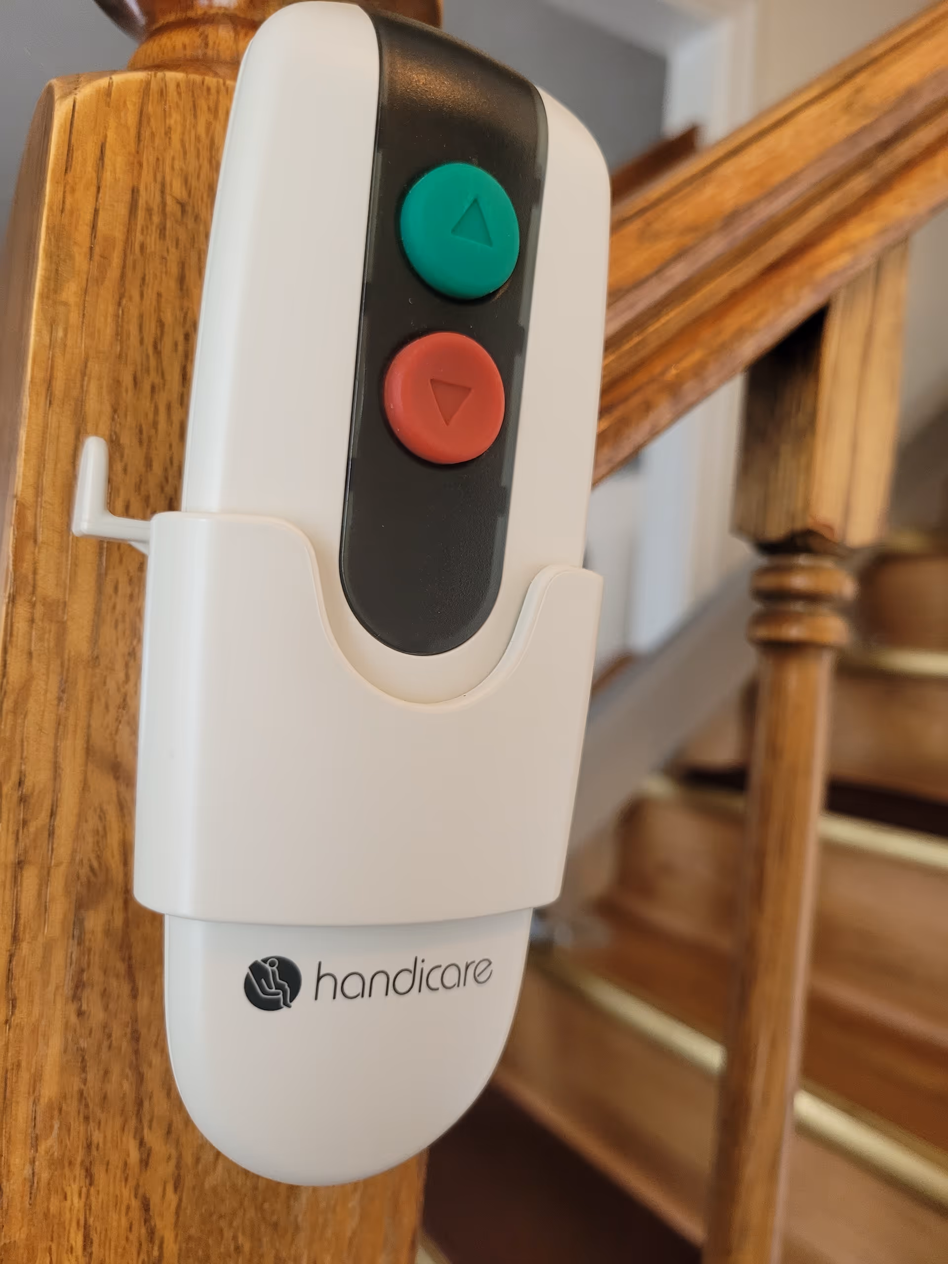 Close-up of a stair lift control with green and red buttons on a wooden banister.
