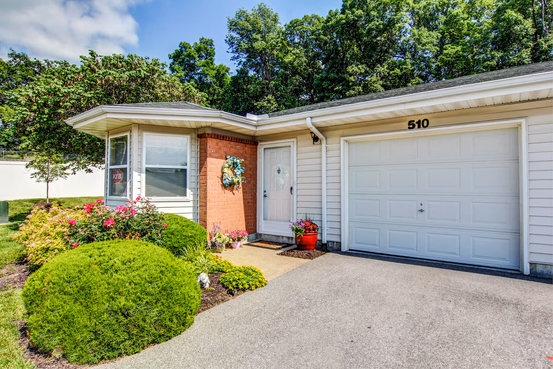 A single-story senior living facility exterior with a front door, garage, and landscaped garden.