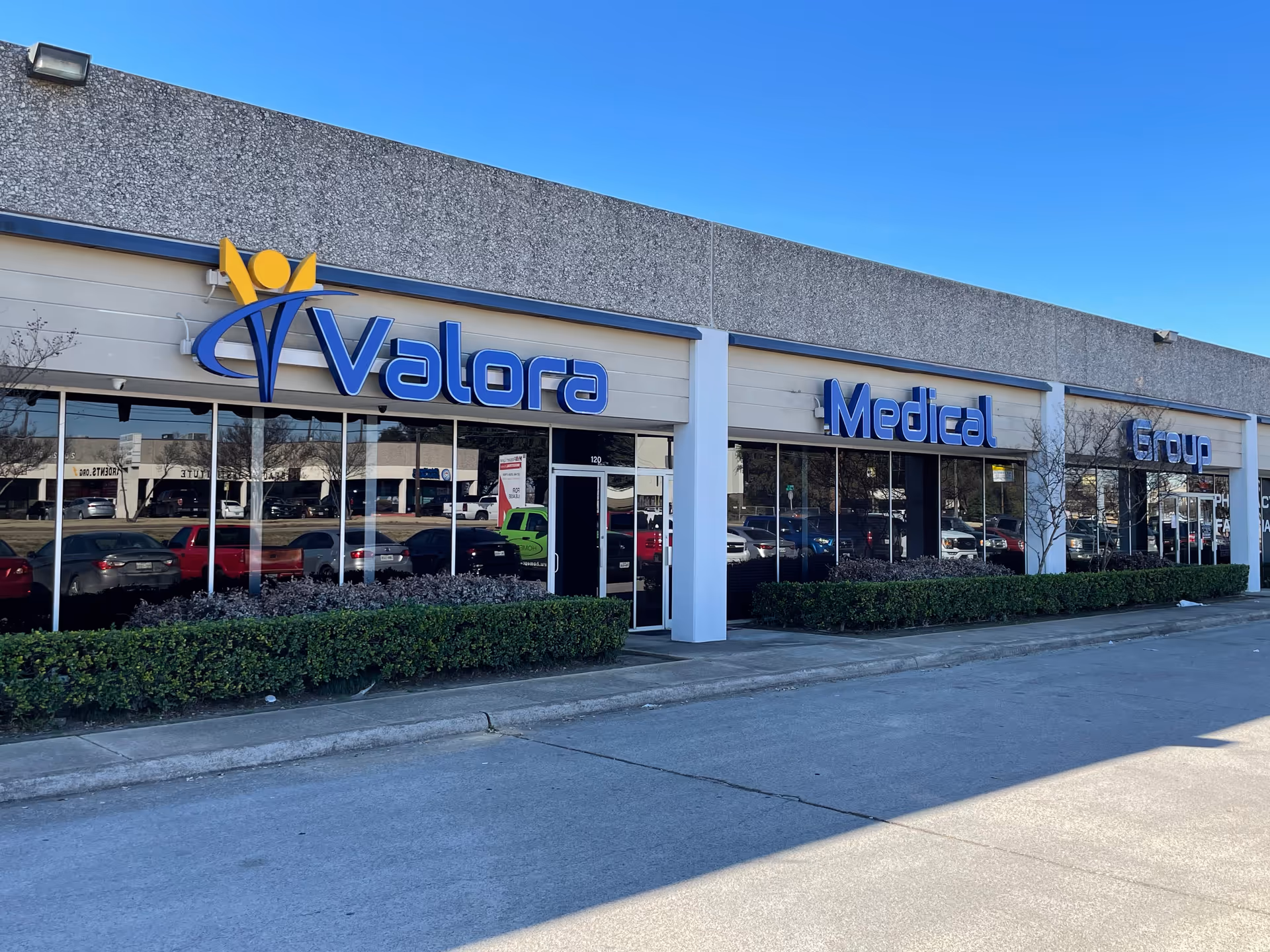 Exterior view of Valora Medical Group Garland storefront with blue sign and parked cars.