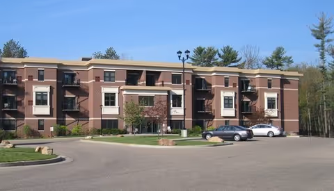 Brick three-story senior living facility exterior with parking lot and manicured landscaping.