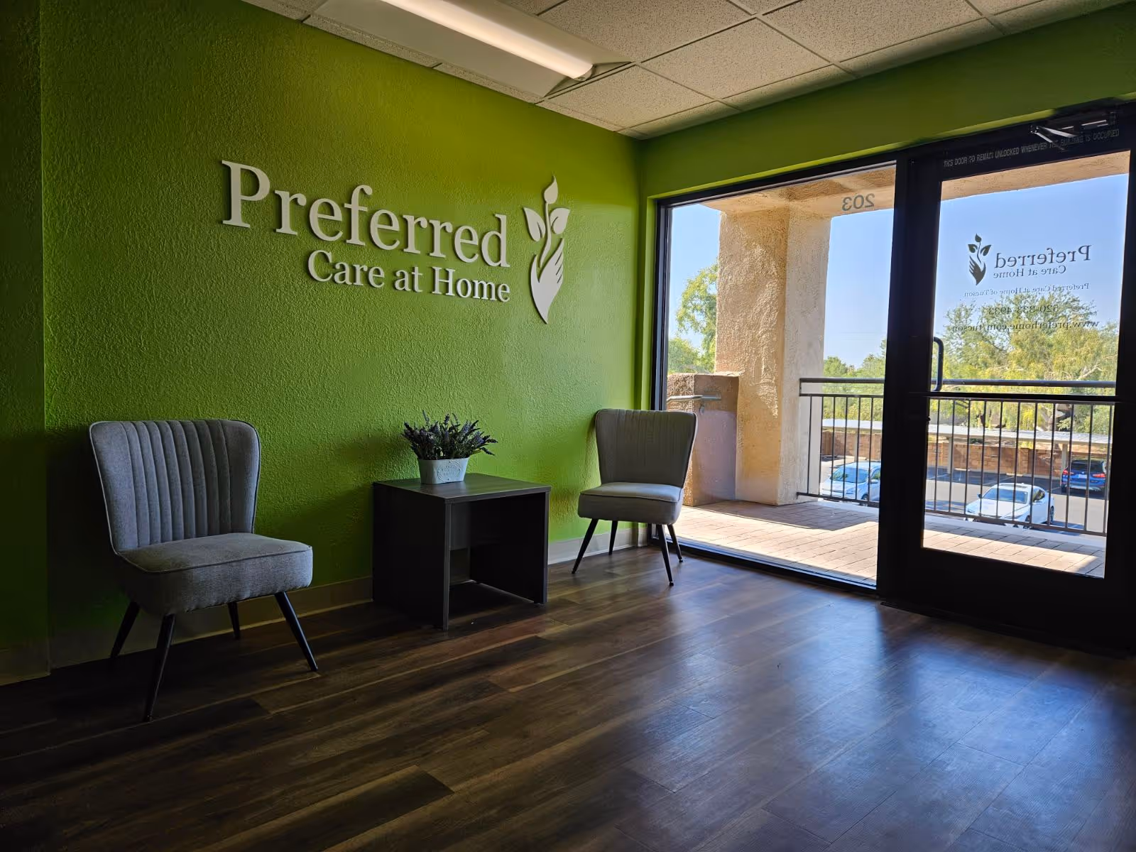 Green-walled lobby with Preferred Care at Home logo, two chairs, small table, and glass doors.