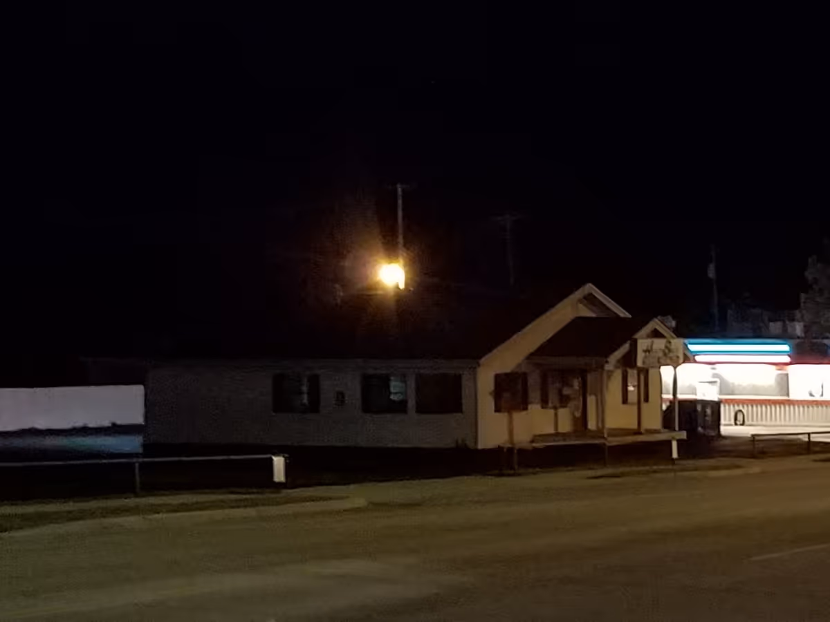 Night exterior of a single-story facility with a lit entrance along a street.
