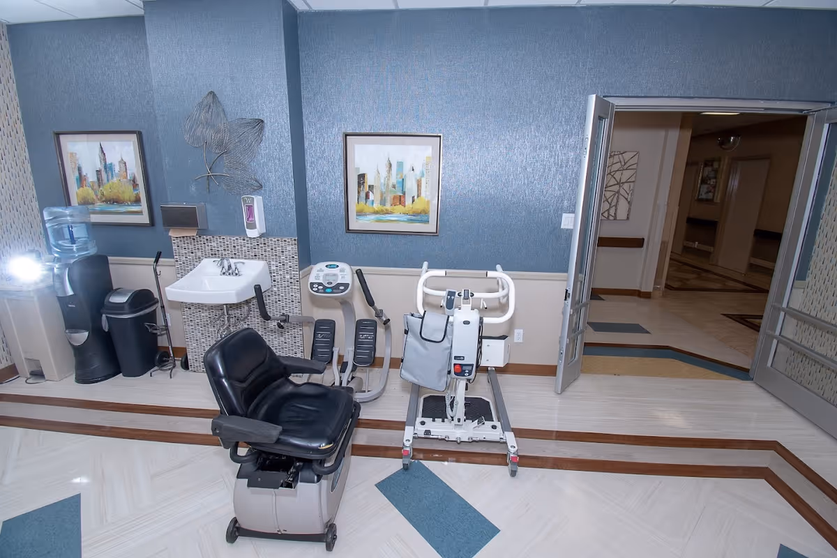 Interior room with medical/rehab equipment including a patient lift, a therapy chair, a recumbent exercise machine, a sink and a water cooler.