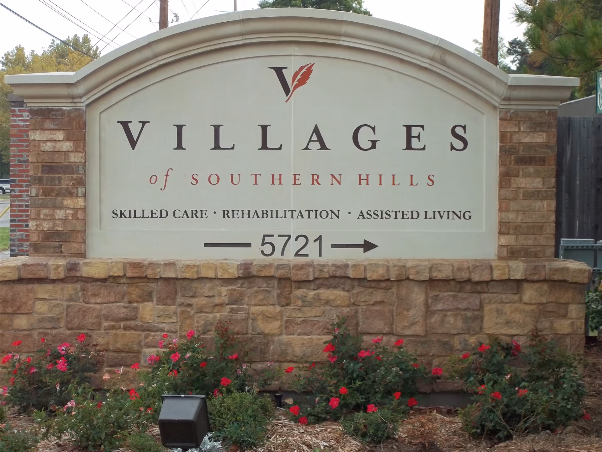 Stone entrance sign reading "Villages of Southern Hills" with services listed and the address 5721, set above a flowerbed.