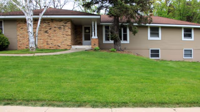 Front view of a single-story senior living facility with brick, beige siding, and a green lawn.