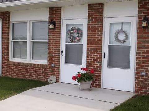 Brick exterior of a senior living facility entrance with wreaths and potted flowers.