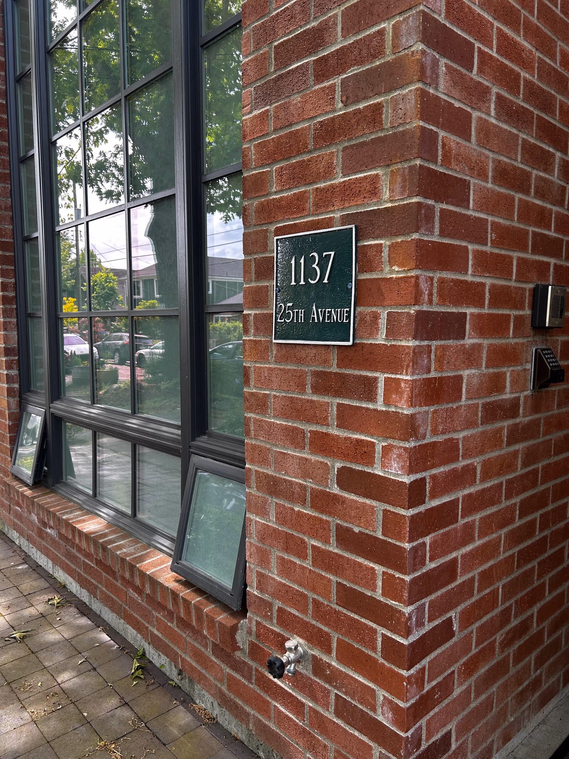 Brick building exterior with large window and a green plaque reading 1137 25th Avenue