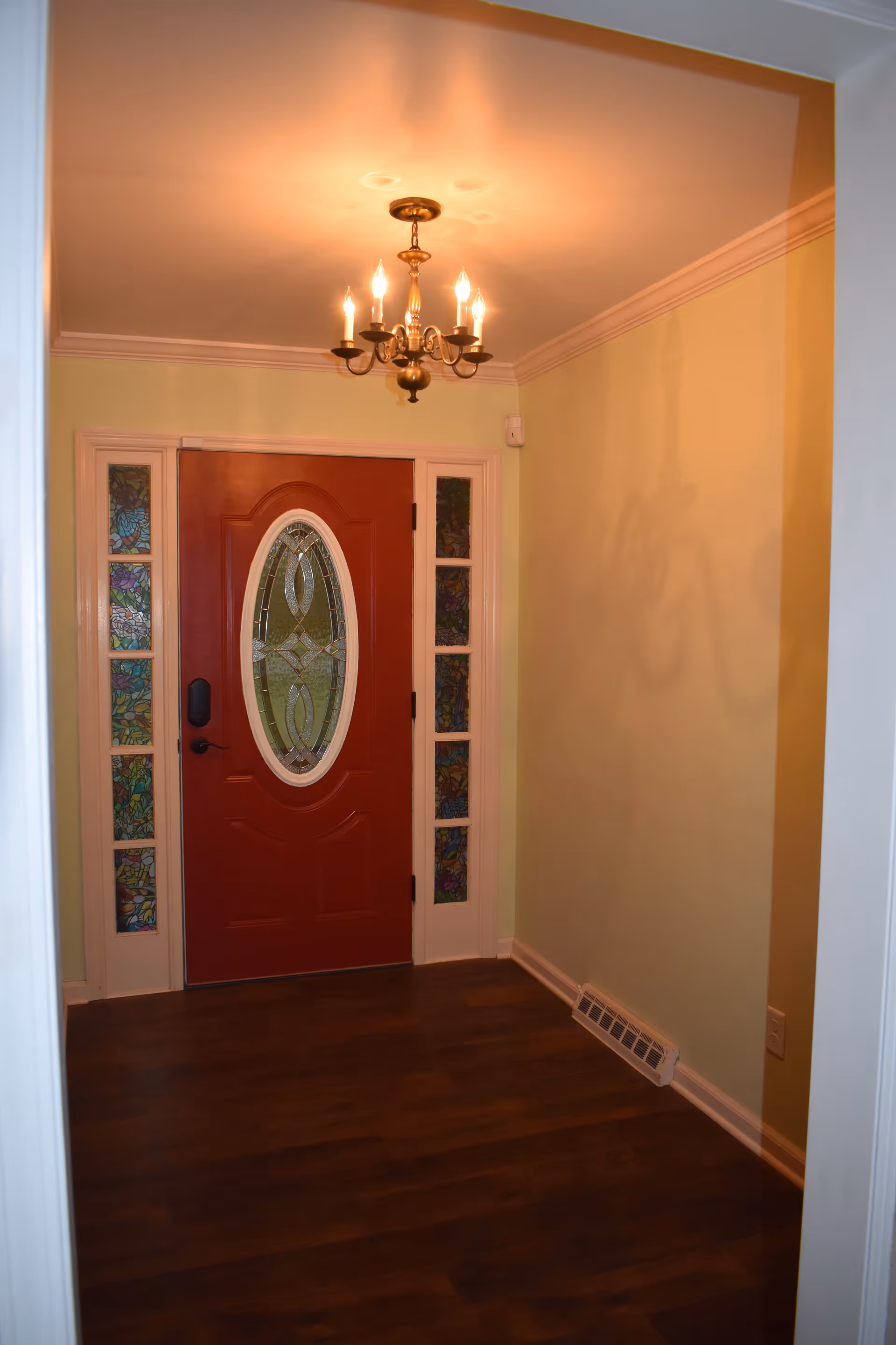 Red front door with oval glass, sidelights, chandelier, and oak floor in entry hall.