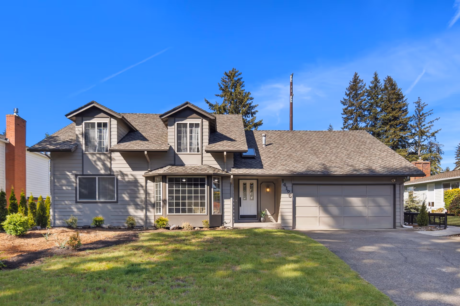 A two-story gray house with a large garage and manicured front yard.