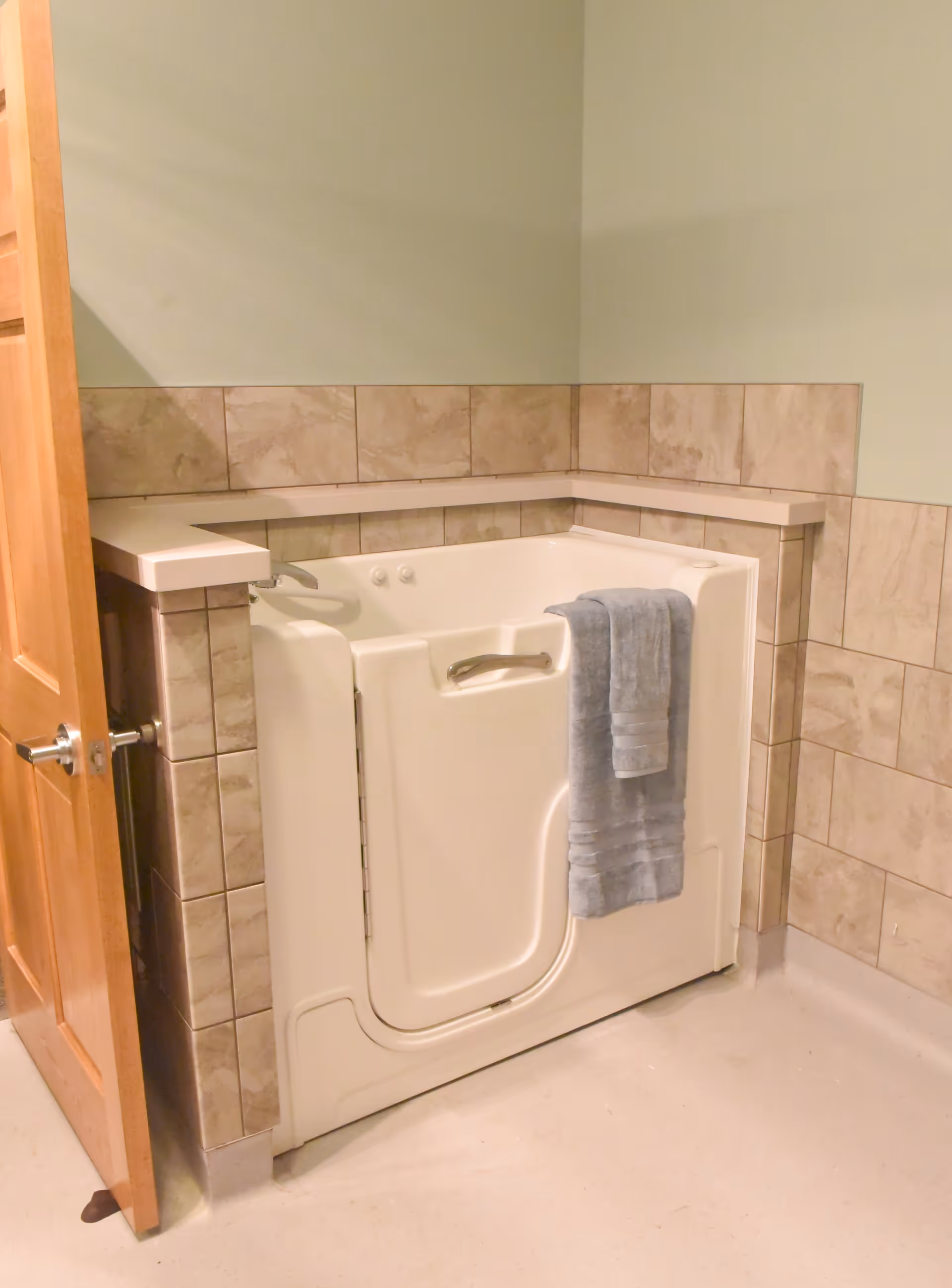 A walk-in bathtub with a hinged door and a towel draped over it set into a tiled bathroom alcove.