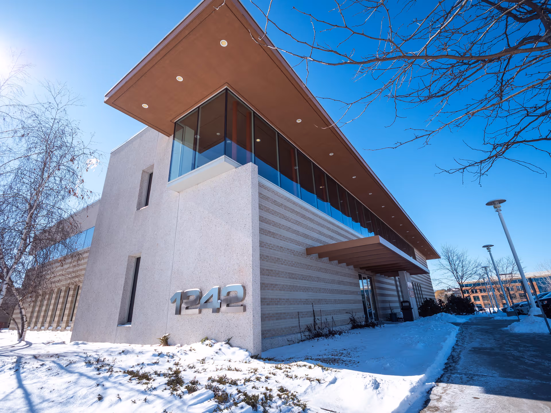 Modern concrete building with glass windows, a brown overhang, and snow around the entrance.