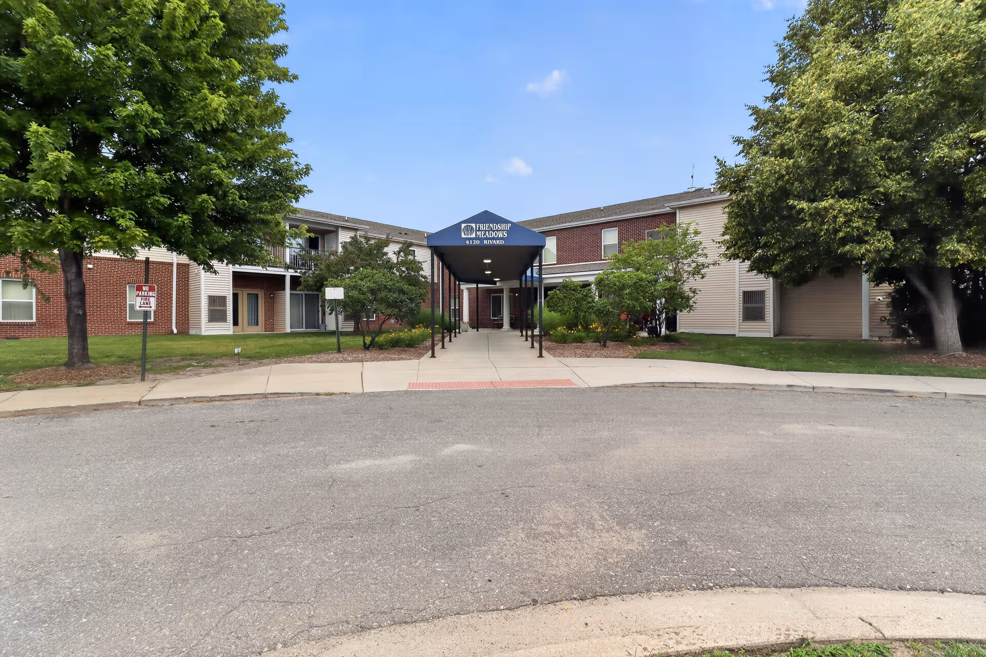 Exterior view of Friendship Meadows Senior Apartments entrance with covered walkway and trees.