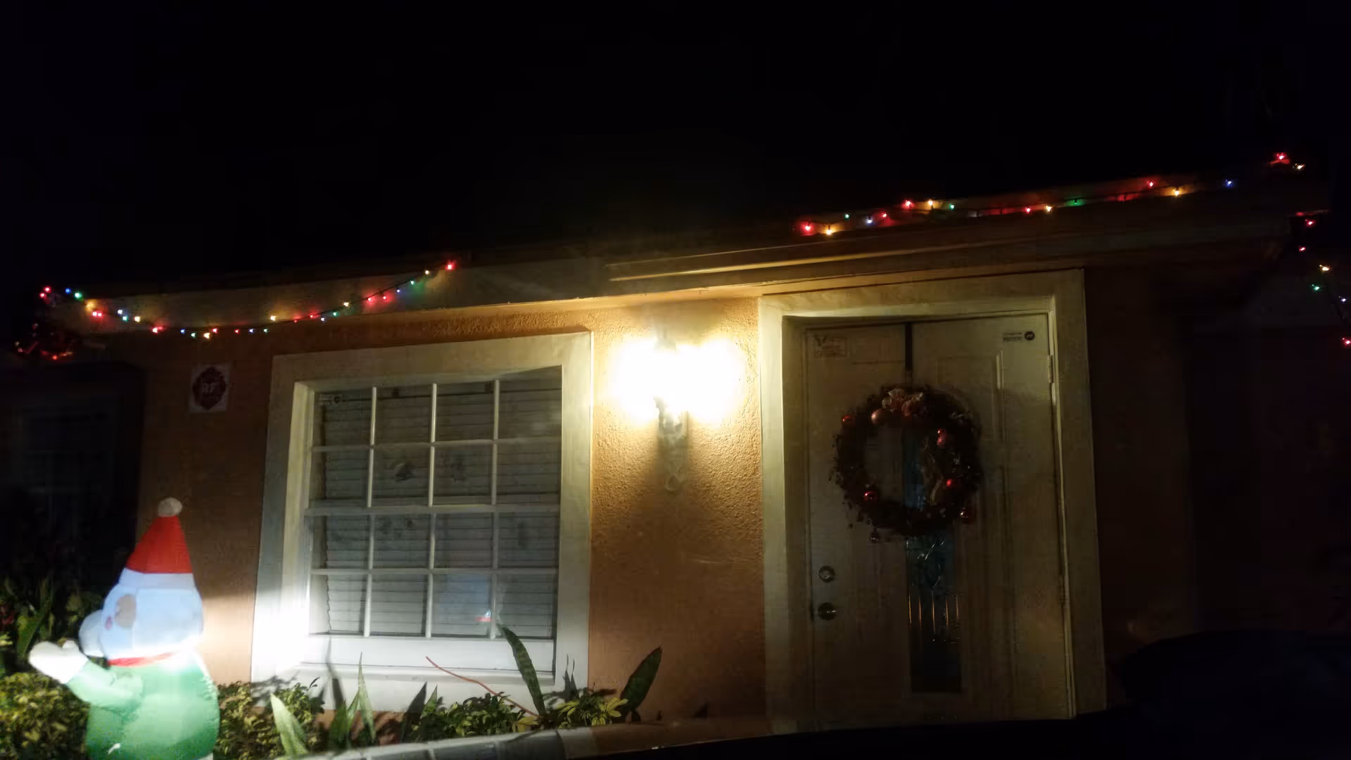 Front entrance of a home with Christmas lights, wreath, window, and Santa figure outdoors at night.