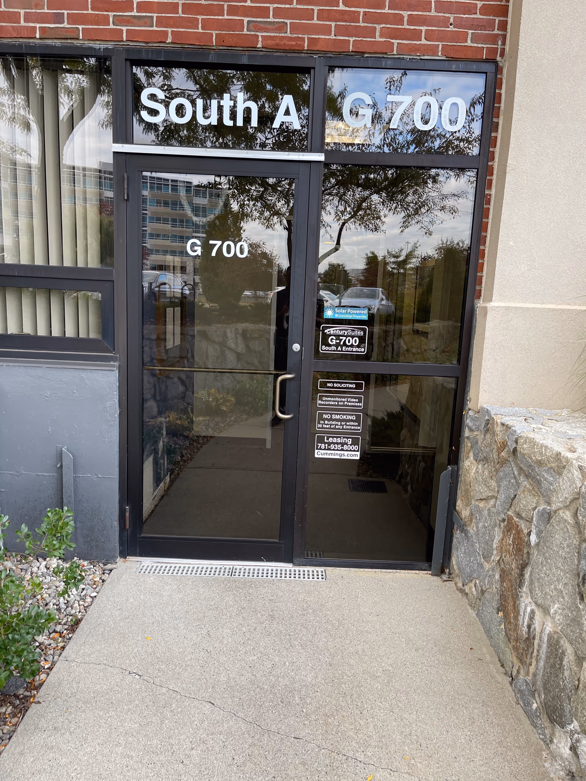 Entrance doors with glass panels labeled South A G-700, brick exterior, and stone wall on side.