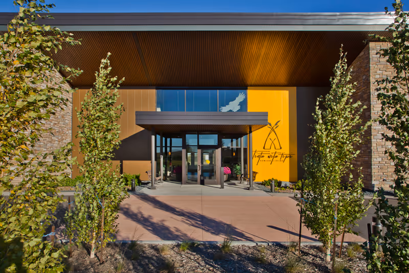 Modern senior living facility entrance with glass doors, orange wall, and landscaped front walkway.