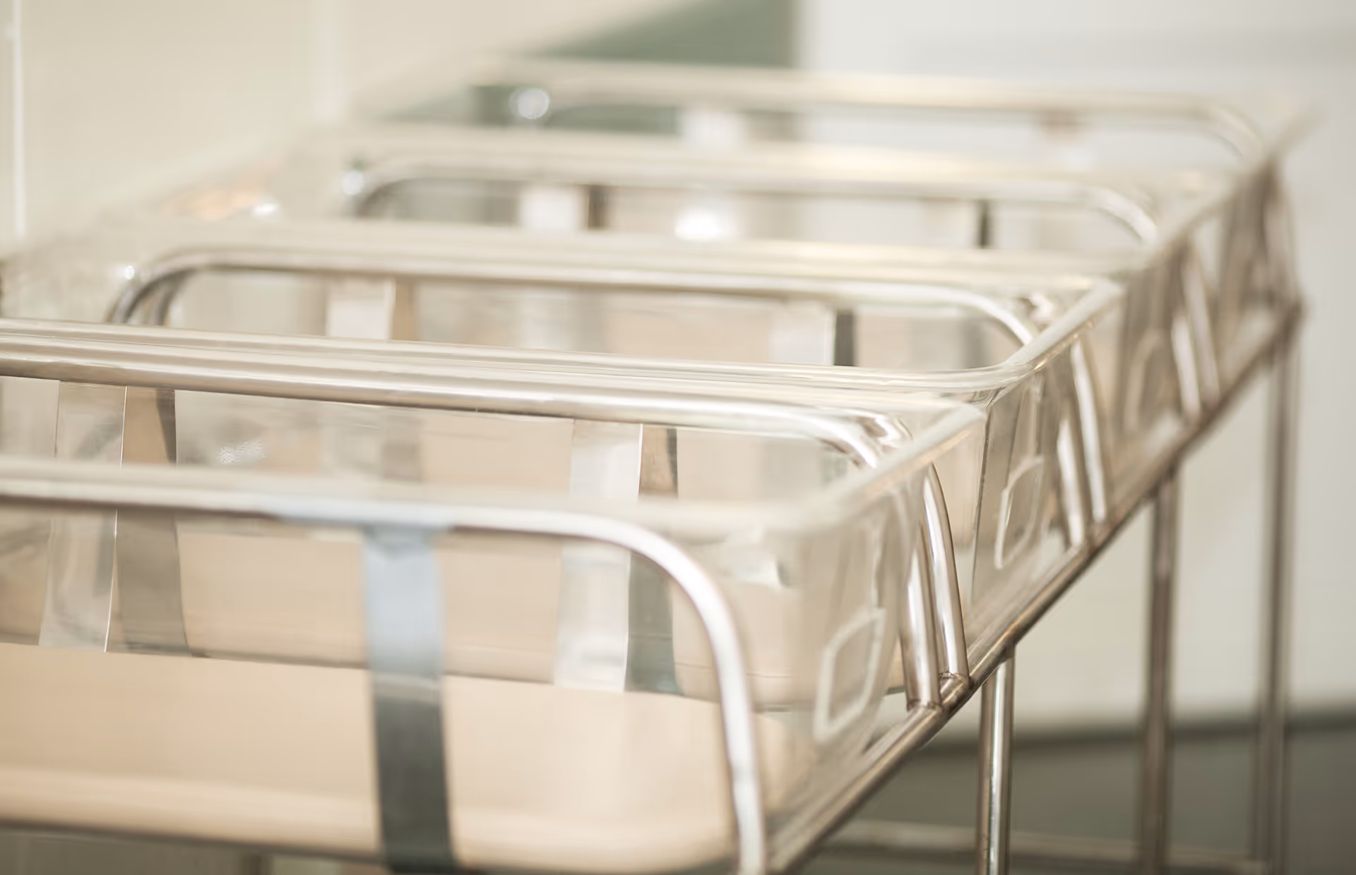 Row of empty stainless steel infant bassinets in a sterile hospital nursery.