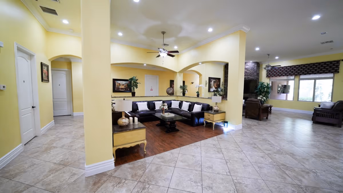 Bright lobby with yellow walls, arched openings, a black sectional sofa, and tiled floor.