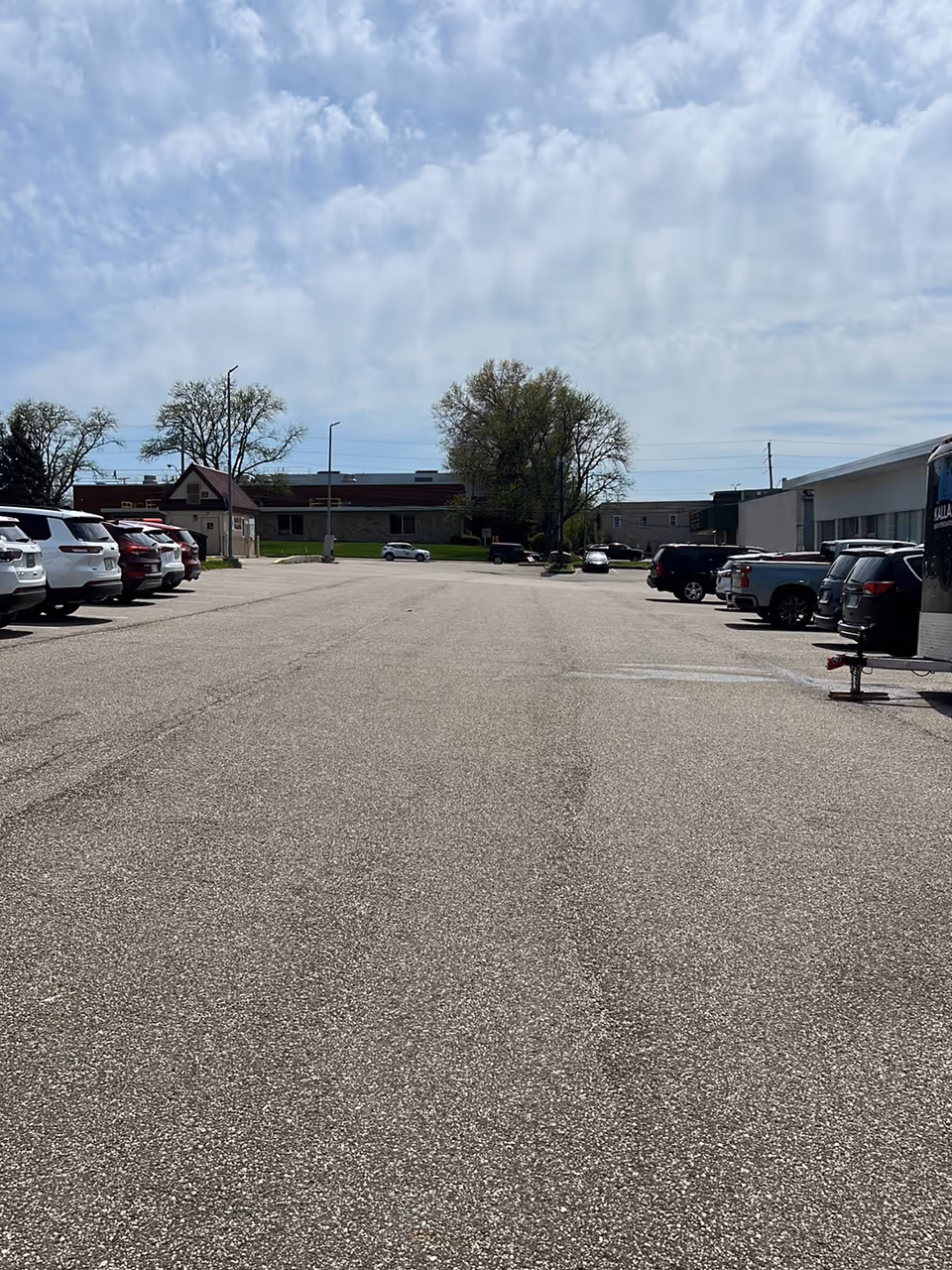Wide view of a parking lot with cars and a distant facility building.