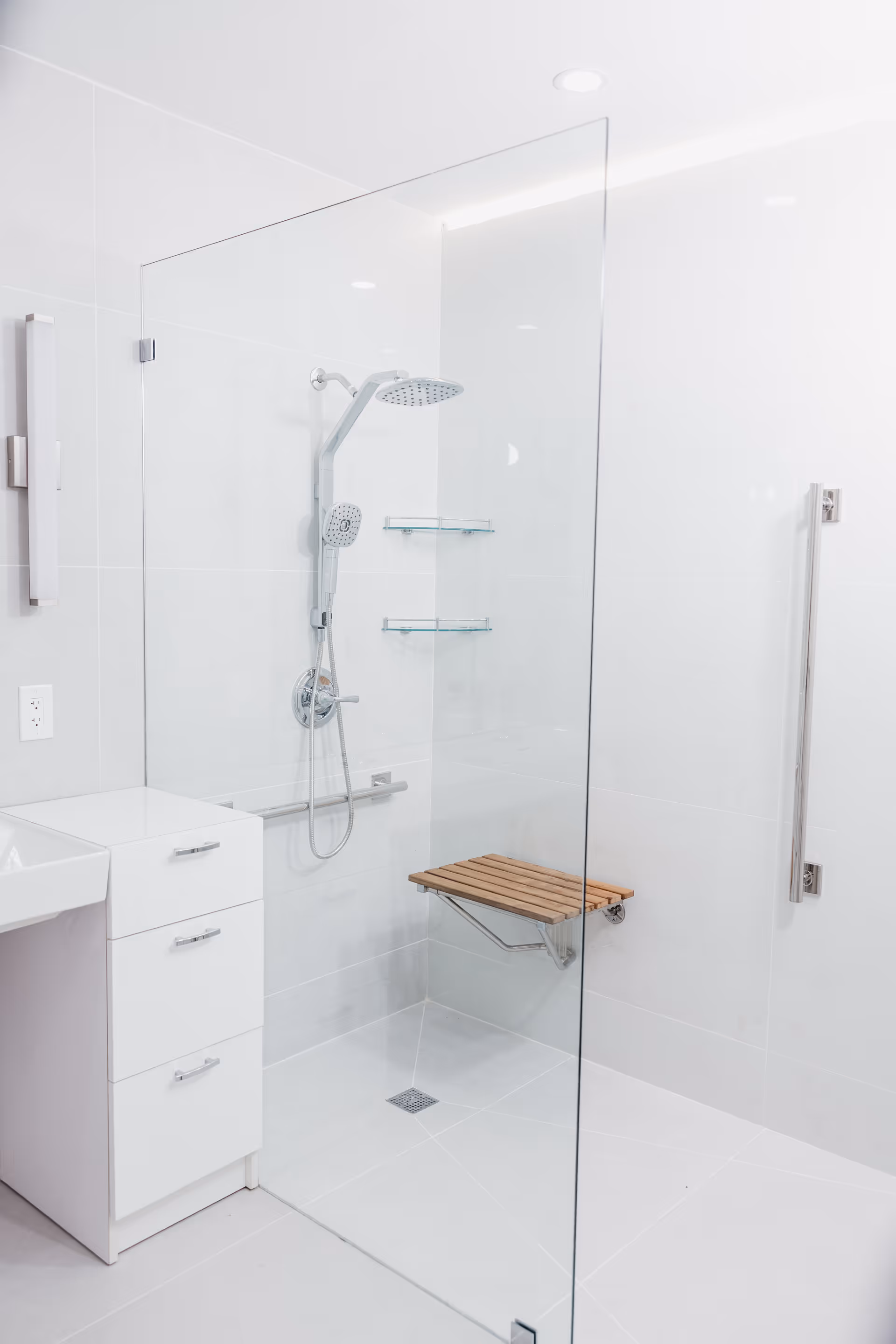 White tiled bathroom with glass shower enclosure, bench, and modern vanity.