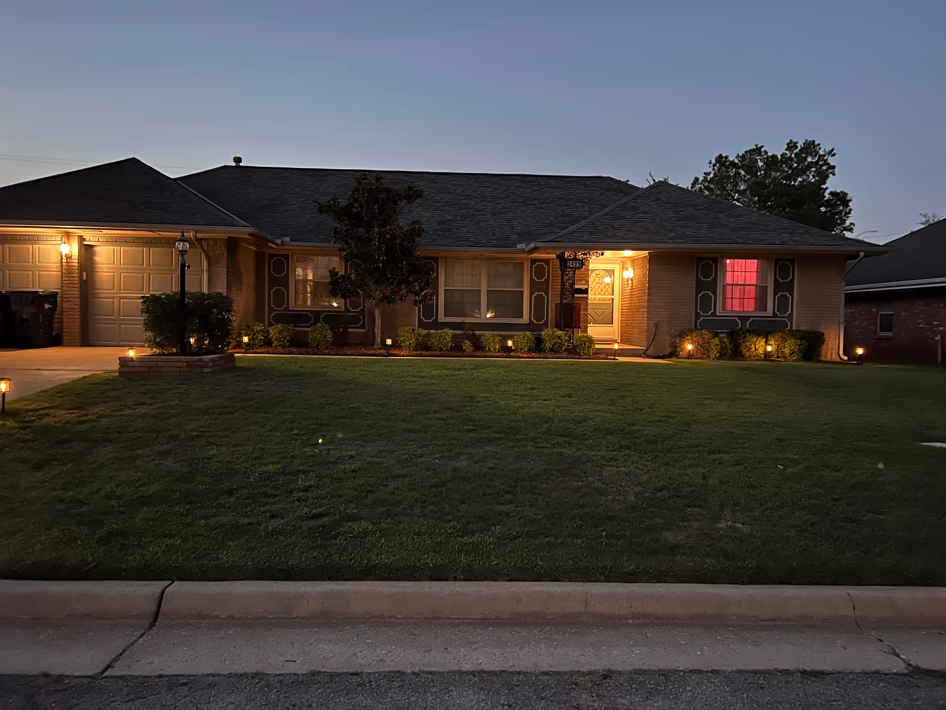Evening exterior view of a single-story building with a lit entrance and well-kept lawn.
