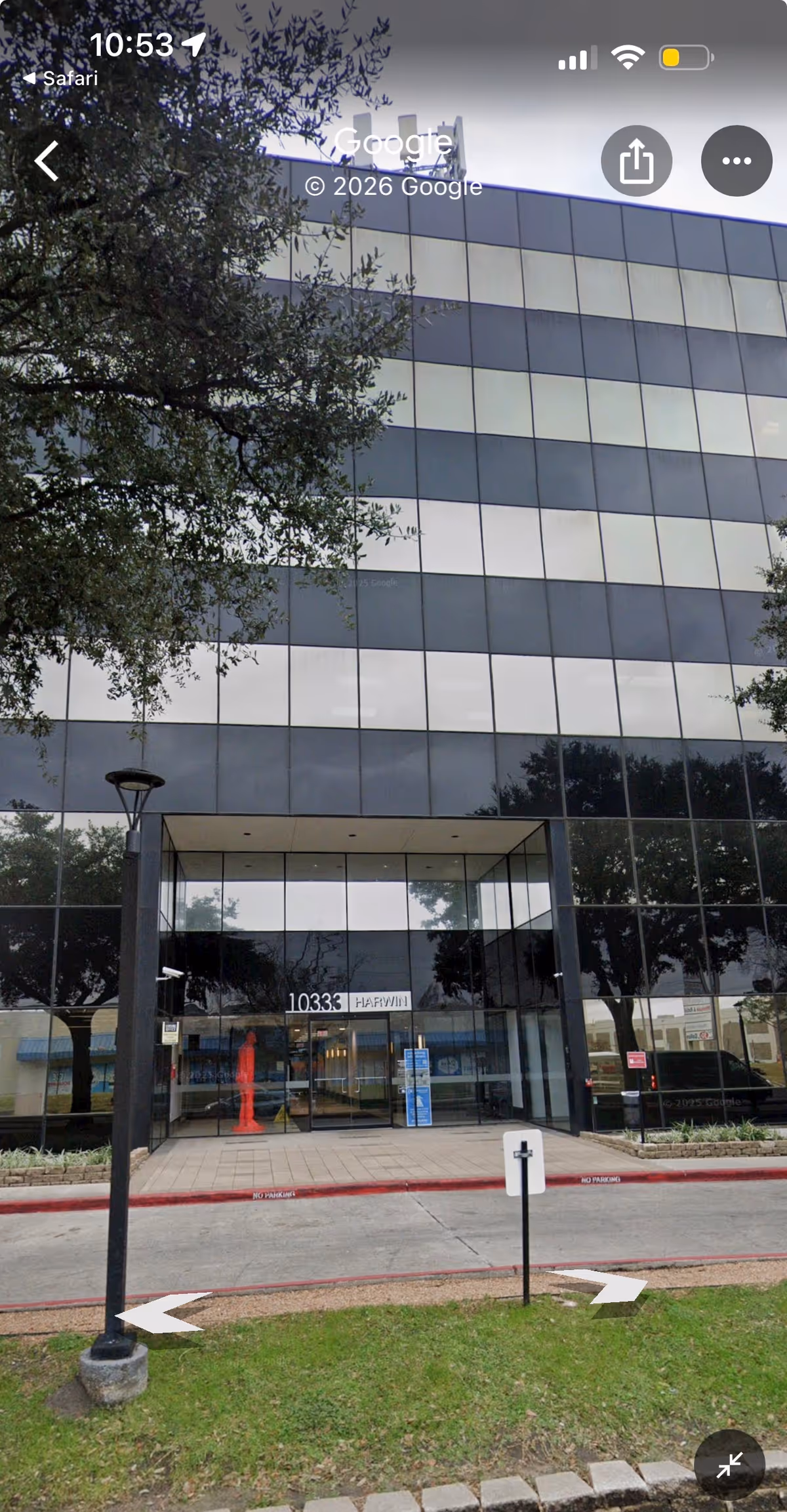 Glass-front building with a wide entrance, trees, and a sidewalk leading to the doors.
