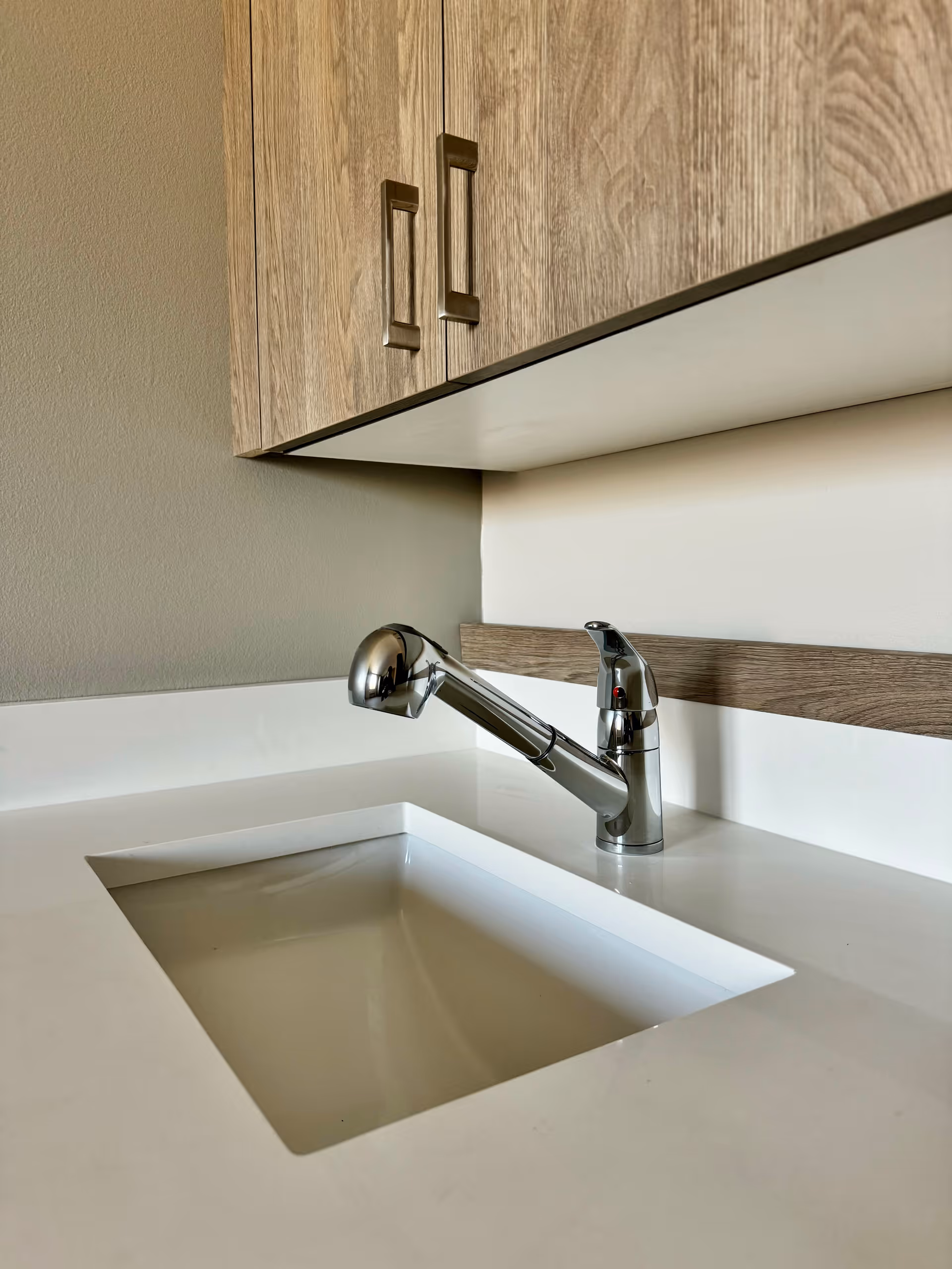 Modern kitchen sink with chrome faucet, white countertop, and wood cabinets.