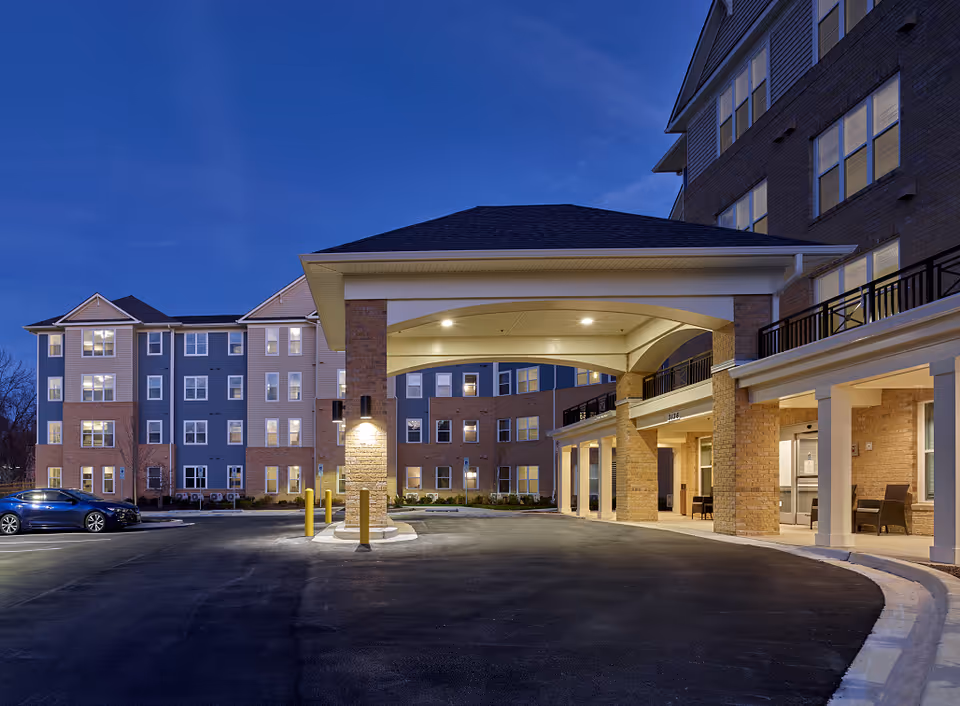 Evening exterior of Pointe View at Aspen Hill, showing the entrance canopy and parked cars.