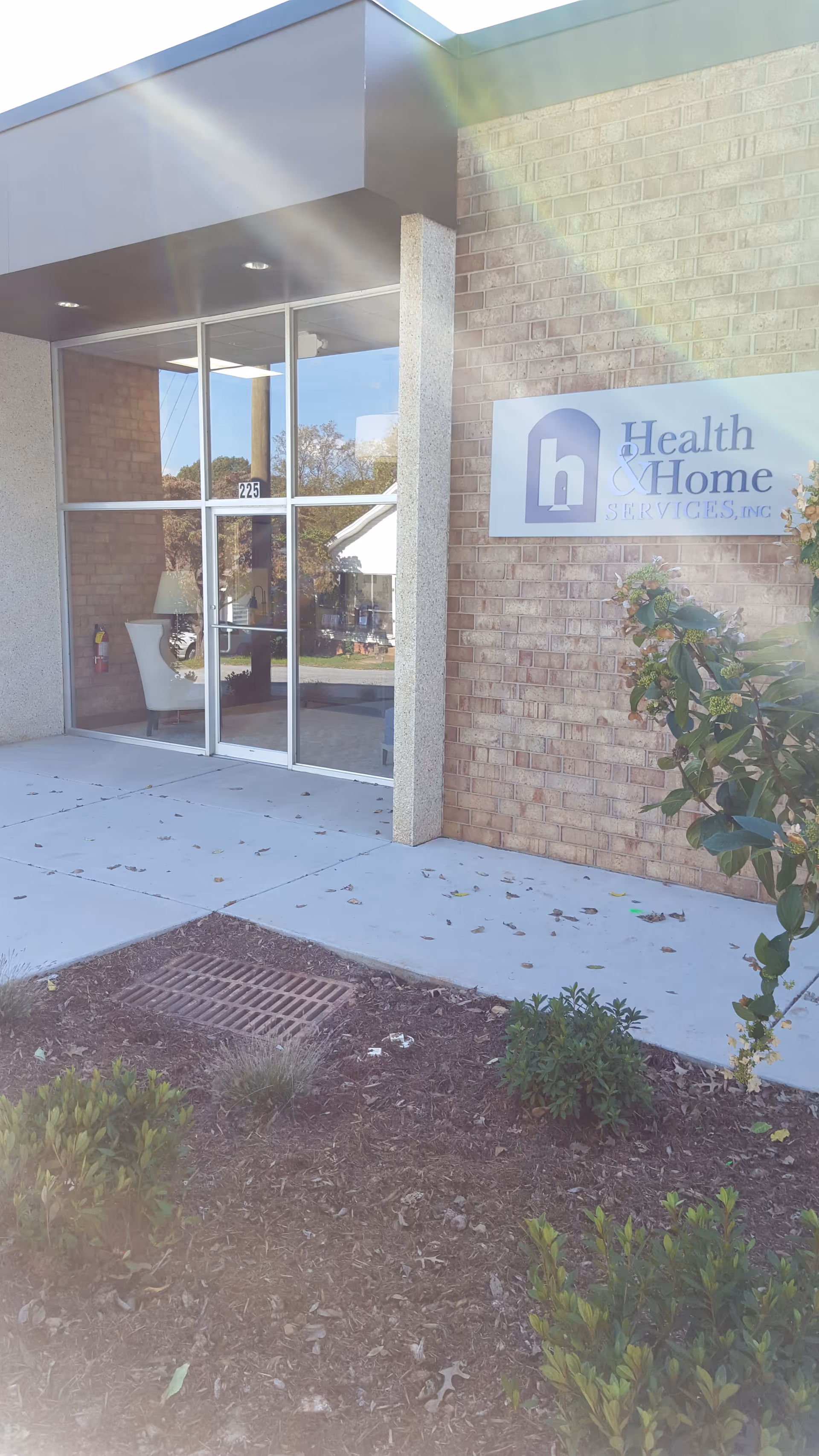 Exterior entrance of Health & Home Services facility with glass doors and sign on brick wall