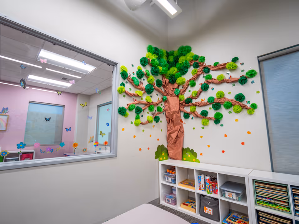 Bright therapy room with a large paper tree mural, colorful decorations, and cubby shelves.