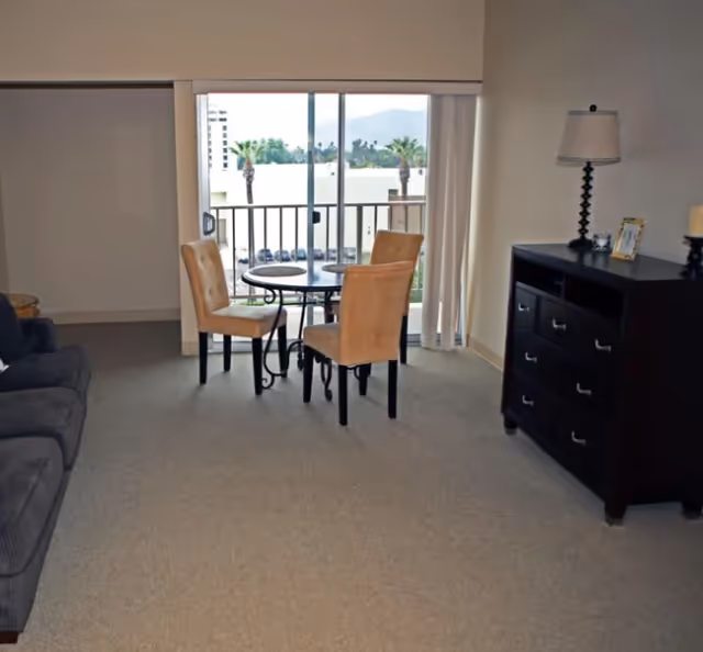 Small living room with round dining table and two chairs by sliding glass door to balcony.